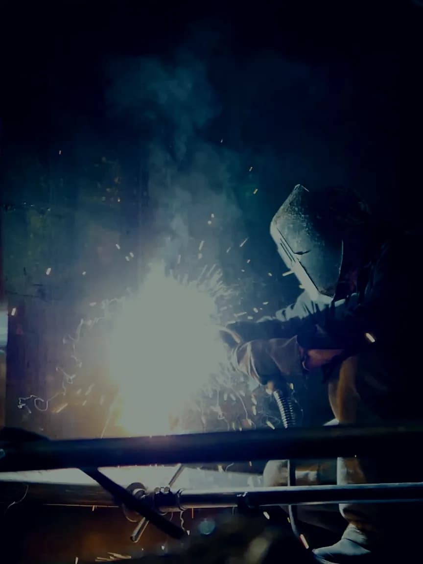 Soldador con careta de protección trabajando entre chispas en un taller industrial